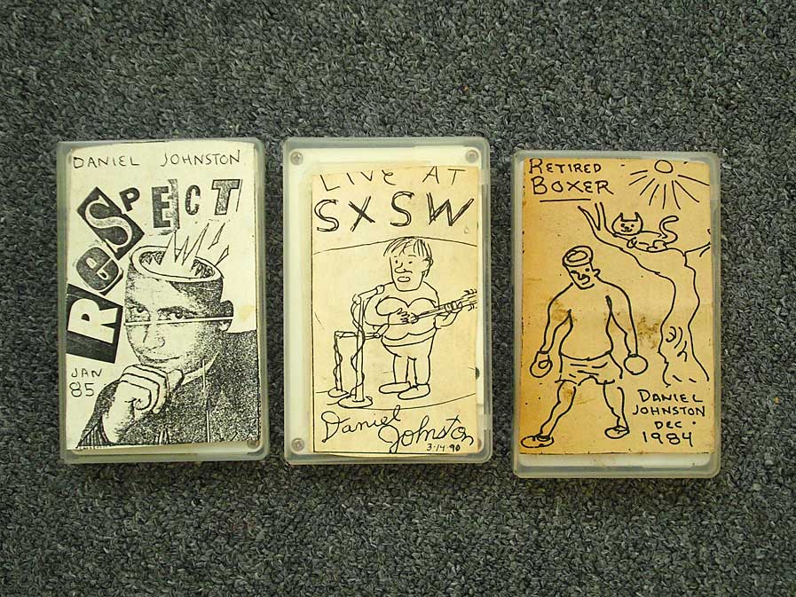 A series of three early Daniel Johnston's cassette tapes adorned with his artwork.